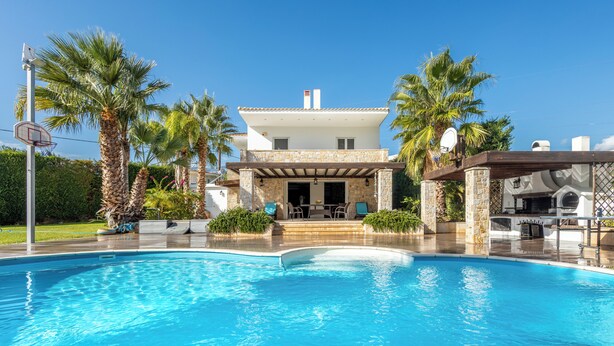 A modern house with a swimming pool, surrounded by palm trees and a patio area.