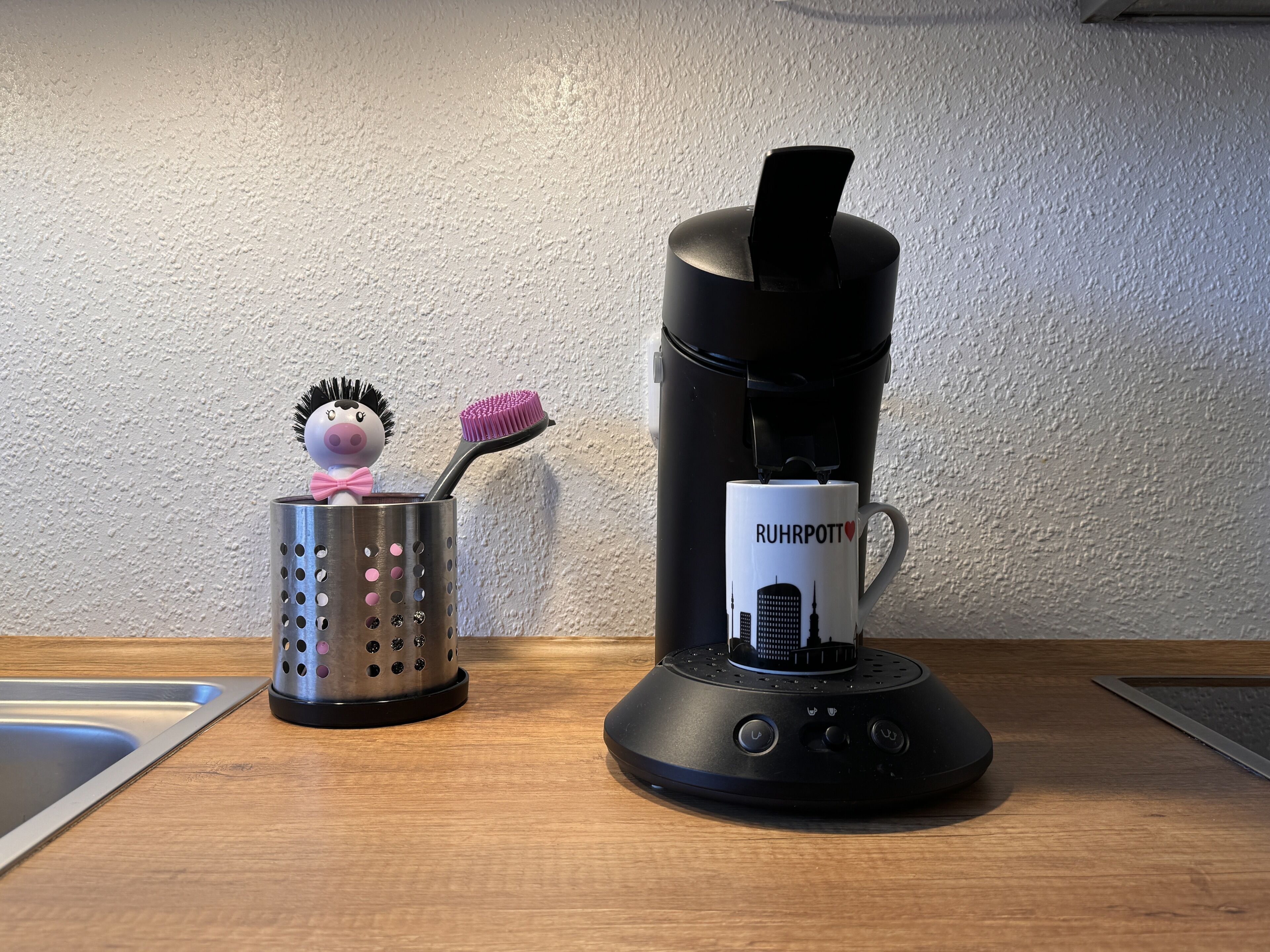 A kitchen counter with a coffee maker, a mug, and a hairbrush holder.