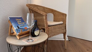 A wicker chair with a cushion, a wine bottle, and a book on a small round table. - Gemütliche, Vollausgestattete Wohnung für 4 Personen im Ruhrgebiet (Castrop-Rauxel)