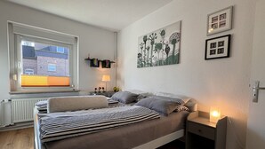 A bedroom with a bed, bedside tables, a window, and wall art. - Gemütliche, Vollausgestattete Wohnung für 4 Personen im Ruhrgebiet (Castrop-Rauxel)