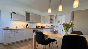A modern kitchen with white cabinets, a wooden countertop, and black chairs. There are pendant lights above the counter and a vase with tulips on the table. - Gemütliche, Vollausgestattete Wohnung für 4 Personen im Ruhrgebiet (Castrop-Rauxel)