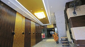 Eine moderne Hotellobby mit einer Wandpaneele aus Holz, einer hellen Deckenleuchte, einem Ventilator und einer kleinen Holzbank.