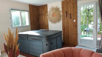 A room with a large hot tub, wooden panel walls, a window with a view of greenery, and a decorative wall piece.