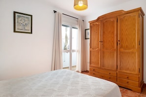 Un dormitorio con cama, armario de madera, ventana con cortinas e iluminación colgante.