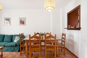 Un comedor con una mesa y sillas de madera, un sofá verde y dos cuadros en la pared.