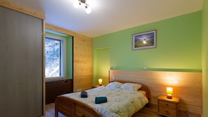 A bedroom with a wooden bed, bedside lamps, a window with a view of trees, and a framed picture on the wall.