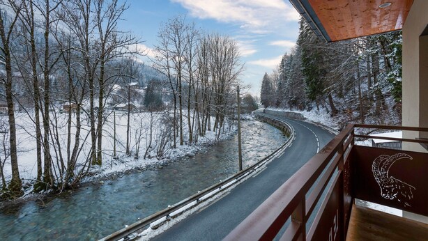 A winter scene with a snow-covered road, a clear stream, and bare trees.