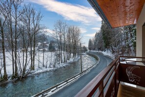 A winter scene with a snow-covered road, a clear stream, and bare trees.