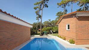 Ein rechteckiger Swimmingpool mit blauen Fliesen, umgeben von Backsteinmauern und einem kleinen Backsteinhaus mit einem Fenster.