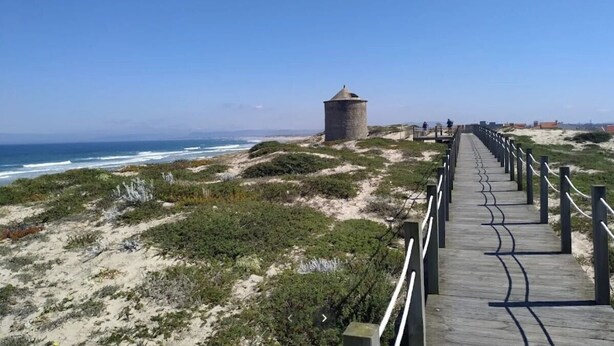 Ein Küstenweg mit einem Turm, sandigem Gelände und Blick auf den Ozean.