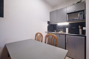 Een kleine keuken met een magnetron, een koelkast en een eettafel met stoelen.