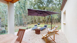 Eine Terrasse im Freien mit Tisch, zwei Loungestühlen, einer Holzbank und einem großen Sonnenschirm.