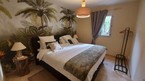 Ein Schlafzimmer mit Bett, Nachttisch, Lampe, einem Fenster mit Vorhängen und einer Pflanzenwand.