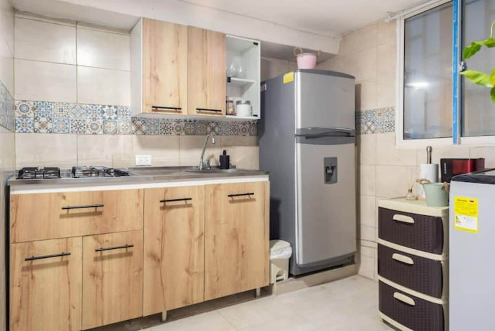 Cozinha com armários de madeira, geladeira de aço inoxidável e painel de azulejos.