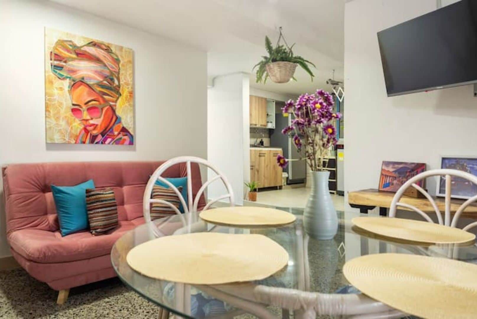 Una sala de estar moderna con un sofá rosa, una mesa de comedor de cristal con individuales tejidos y un jarrón de flores.