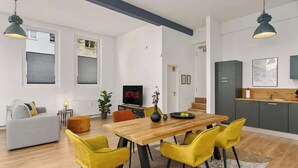 A modern living room with a wooden dining table, yellow chairs, a grey sofa, and a TV displaying 'NETFLIX'.
