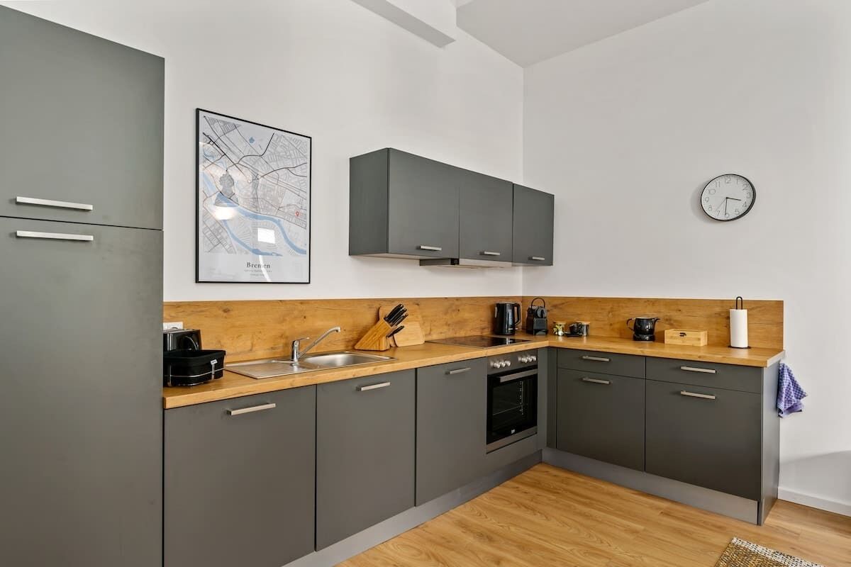 Een moderne keuken met grijze kastjes, een houten aanrecht, een kaart en een klok.
