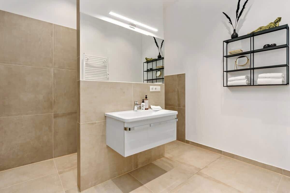 A bathroom with a white sink, a mirror, and a shelf with toiletries.