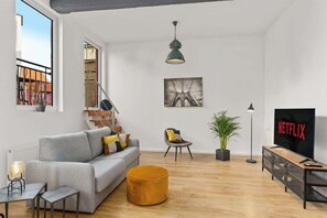 Een moderne woonkamer met een grijze bank, een rond hocker, een televisie en een boekenkast.