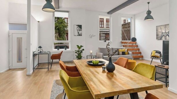A modern living room with a wooden dining table, yellow chairs, and a staircase. - MEL&BENS Loft 2 | Terrace | Design | Weserstadion (Bremen)