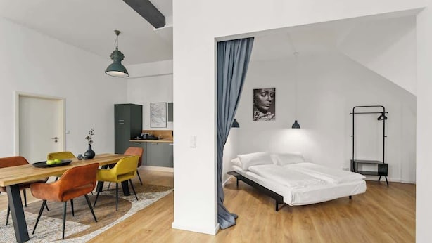 A modern apartment with a dining area, a bed, and a small kitchenette. - MEL&BENS Loft 1+2 for 8 P. | terrace | sauna | Design | Weserstadion (Bremen)