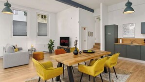 A modern living room with a wooden dining table, yellow chairs, a grey sofa, and a TV displaying 'NETFLIX'. - MEL&BENS Loft 1+2 for 8 P. | terrace | sauna | Design | Weserstadion (Bremen)