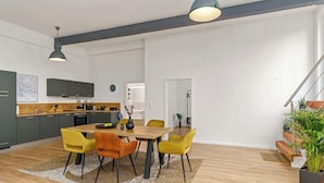 A modern kitchen with dark cabinets, a wooden dining table, and yellow chairs. - MEL&BENS Loft 1+2 for 8 P. | terrace | sauna | Design | Weserstadion (Bremen)
