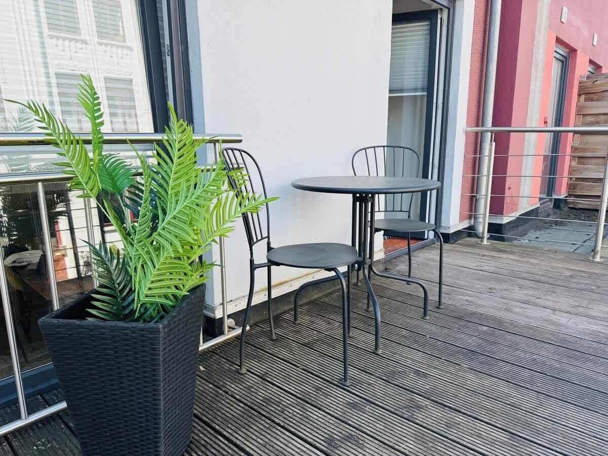 A balcony with a wicker planter, two chairs, and a small round table.