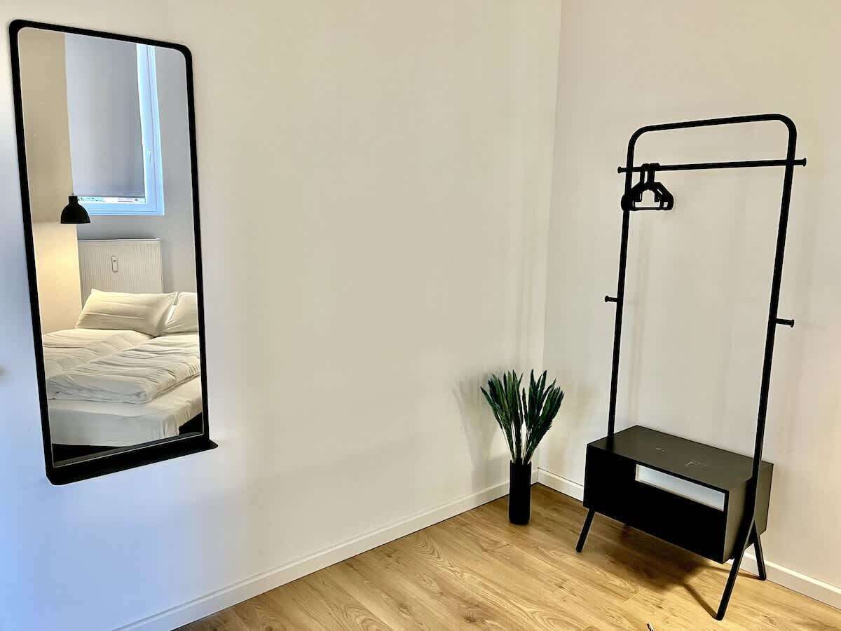 A room with a bed, a mirror, a small plant, and a black metal stand.