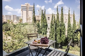 A balcony with a table set with fruits, overlooking a cityscape with buildings and trees.