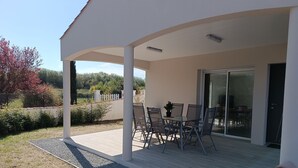 A covered patio with a table and chairs, a sliding glass door, and a view of a landscaped garden. - Charming 6-Person Cottage Near Ocean & Cycling Routes (Beauvoir-sur-Mer)