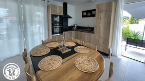 A modern kitchen with wooden cabinets, a black stove, and a dining area with a round table and chairs. - Charming 6-Person Cottage Near Ocean & Cycling Routes (Beauvoir-sur-Mer)