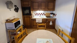 A compact kitchen with wooden cabinets, a microwave, a coffee maker, and a dining table with chairs. - Cozy 2-BR Apt for 6 Near Pool, Ski Bus & Amenities (Les Carroz d'Arâches)