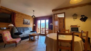 A cozy cabin-style room with a wooden interior, a sofa, a dining table, and a television. - Cozy 2-BR Apt for 6 Near Pool, Ski Bus & Amenities (Les Carroz d'Arâches)