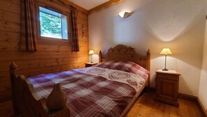A cozy bedroom with a wooden bed, two bedside tables with lamps, a window with curtains, and a wooden headboard. - Cozy 2-BR Apt for 6 Near Pool, Ski Bus & Amenities (Les Carroz d'Arâches)