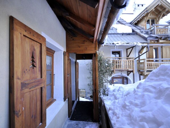 A wooden building with a snow-covered ground, a wooden door with a window, and a balcony with railings.