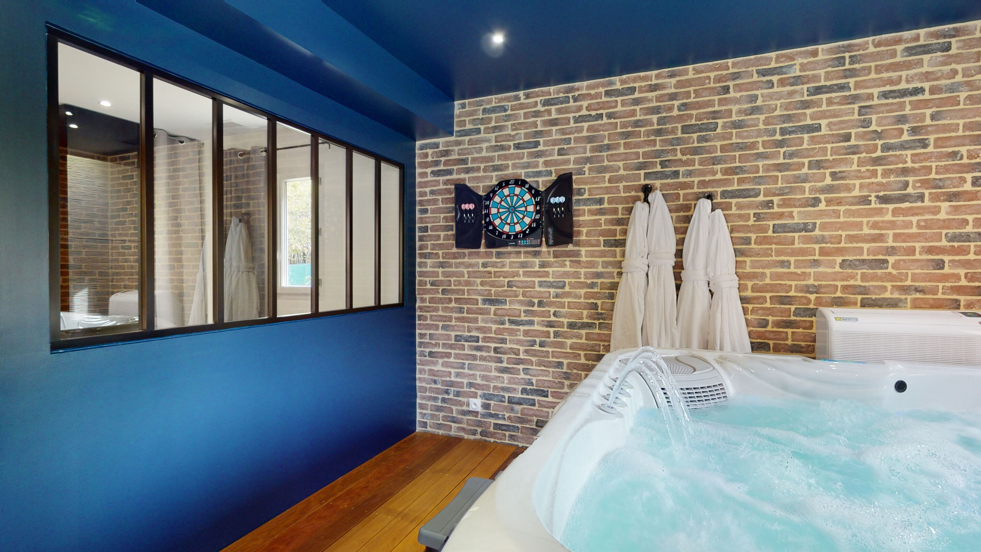 A room with a brick wall, a dartboard, and two white towels hanging on hooks.