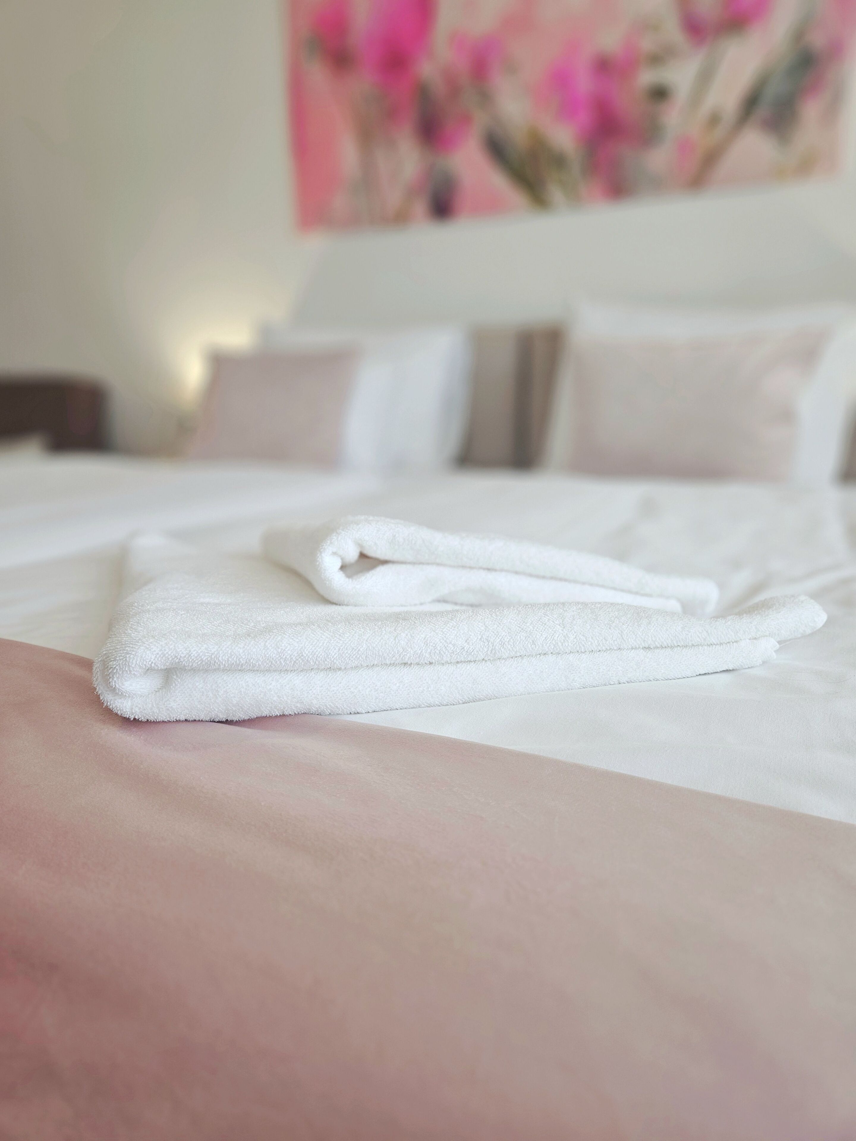 A neatly made bed with white linens and a folded towel on the side.
