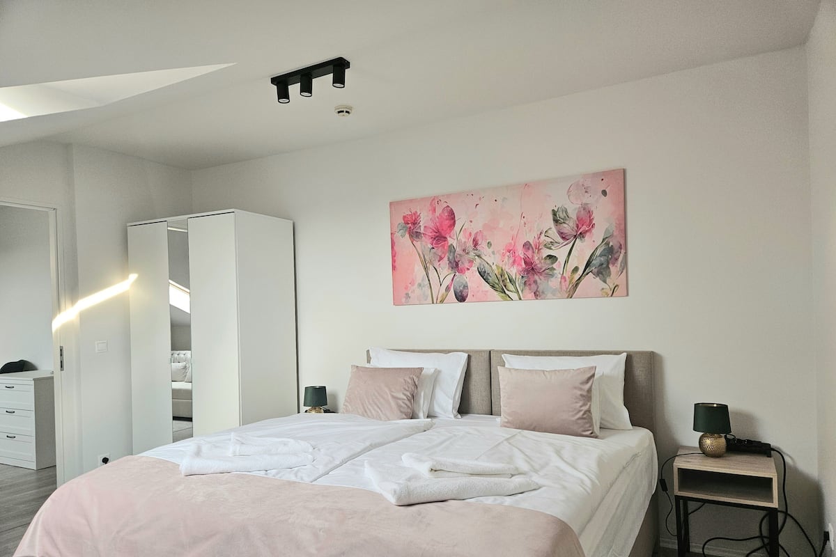 A modern bedroom with a large bed, bedside tables, a wardrobe, and a painting on the wall.