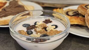 Un bol de yaourt garni de granola et de myrtilles, entouré de diverses pâtisseries et de pains.