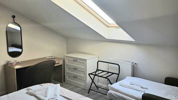 Une chambre d’hôtel avec une lucarne, un lit, un bureau, une commode et une chaise.