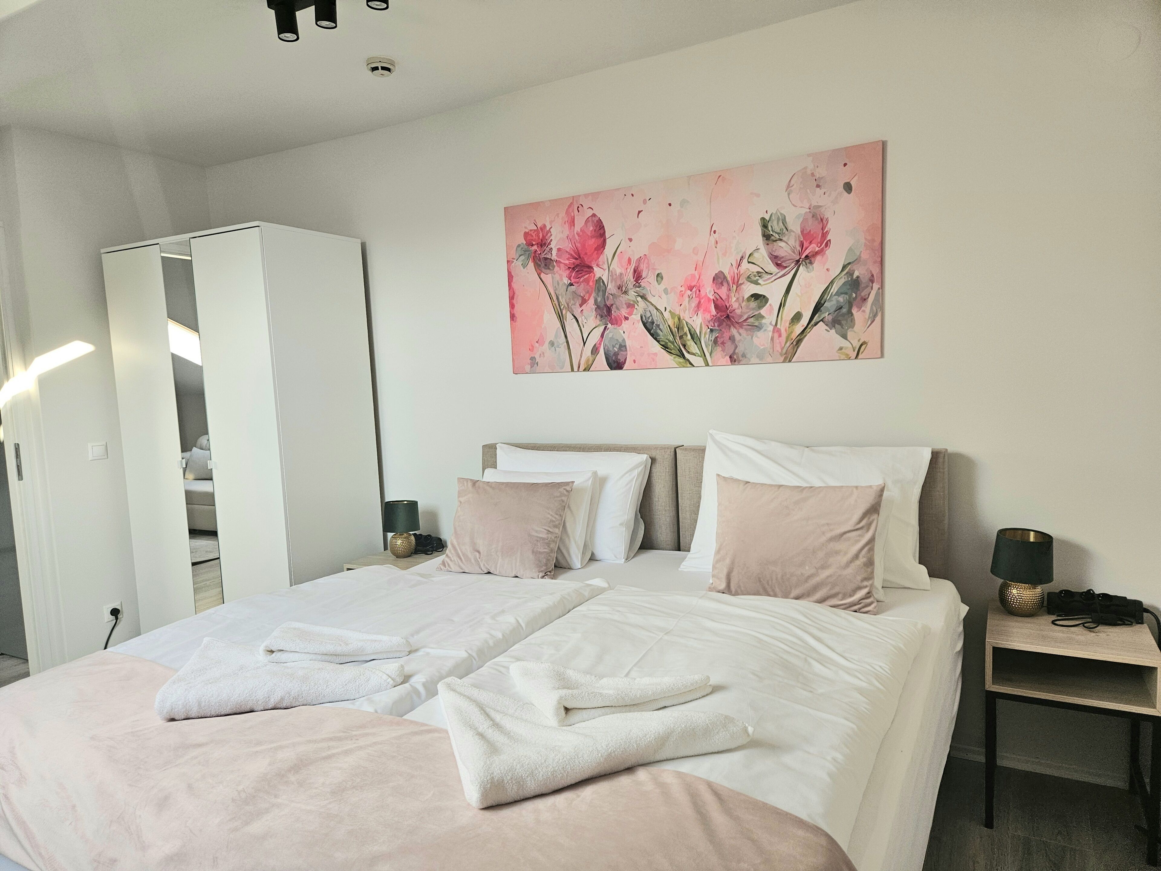 A bedroom with a bed, pillows, a nightstand, a lamp, and a painting on the wall.
