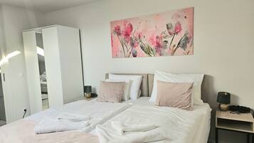 A bedroom with a bed, pillows, a nightstand, a lamp, and a painting on the wall.