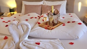 A hotel room with a bed adorned with rose petals, a bottle of champagne, and two glasses. - Holdvirág Hotel (Sarvar)