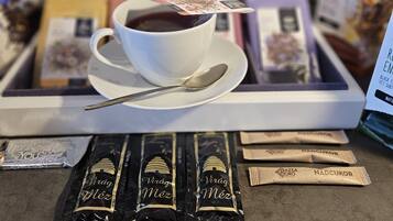 Une tasse de café sur un plateau, accompagnée de plusieurs dosettes de café étiquetées « Virág Méz » et « NADCUKOR », devant un présentoir coloré rempli de dosettes de café.
