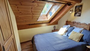 Ein Schlafzimmer mit schrägen Wänden, einem Oberlicht, einem Bett mit blauer Bettwäsche und einem hölzernen Kopfteil.