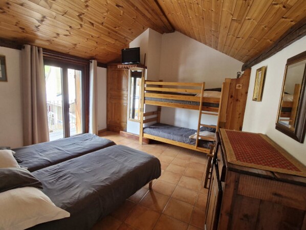 A room with two beds, a bunk bed, wooden ceiling, and a window with curtains.
