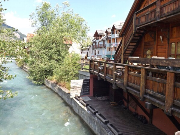 Un pont en bois enjambe une rivière, avec des bâtiments situés sur la rive droite.
