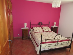 Une chambre à coucher avec un lit, deux tables de chevet, une commode, une armoire en bois et un mur rose.