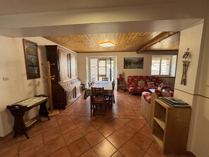 A dining area with a wooden ceiling, a dining table with chairs, a red patterned sofa, and a wooden cabinet.